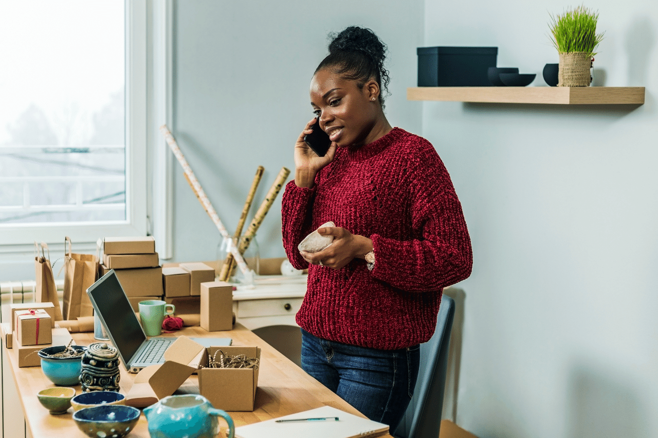 Woman business owner standing at her desk on her phone.| Purely Write